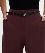 Pantalón carrot sastrero de corte recto y cintura alta, confeccionado en crepé. Presenta trabillas en la cintura, cierre tradicional y bolsillos traseros decorativos. Incluye un cinturón fino de material sintético.