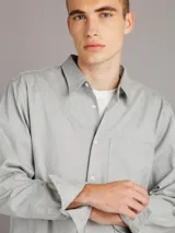 Camisa gris melange de manga larga con cuello clásico, cierre frontal con botones, bolsillo de parche en el pecho y corte recto.