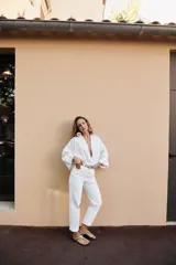 Camisa de lino color blanco con cuello solapa, escote en pico y cierre frontal con botones. Presenta mangas anchas de largo tres cuartos con dobladillo y bajo asimétrico.