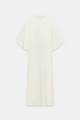 Vestido midi de corte fluido, color crudo, con cuello alto y mangas cortas tipo capa. Presenta un diseño minimalista con bajo recto y aberturas laterales, con cierre en la espalda.