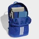 Mochila Adidas modelo Tiro, color azul con detalles en blanco. Cuenta con compartimento principal con cierre, bolsillos laterales de malla y correas acolchadas ajustables. Presenta el logo de la marca en la parte superior y las tres tiras características en la parte inferior frontal.