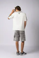 Remera tipo chomba de tejido de punto color blanco, con cuello polo y diseño de rayas verticales sutiles. Presenta estampado gráfico frontal con texto y logo, además de detalles de rayas negras en los hombros.