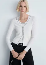Cardigan de punto canalé color blanco, con cuello en V y cierre frontal de botones. Presenta un diseño ajustado con ribetes en contraste negro en el cuello y la botonera.
