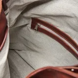 Cartera tipo hobo de cuero con textura granulada, diseño holgado y correa larga ajustable. Presenta un detalle de tira decorativa frontal con hebilla metálica y logo de la marca grabado en la parte inferior.