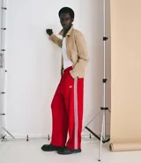 Pantalón deportivo de corte holgado en color rojo, con cintura elástica, bolsillos laterales y franjas verticales blancas a los costados. Presenta un pequeño logo estampado en la parte superior.