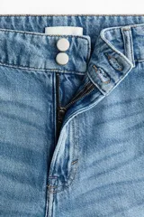 Jean de tiro alto en denim de algodón rígido, con diseño de pierna ancha y corte holgado desde el muslo hasta el bajo. Presenta cierre frontal con doble botón, bolsillos laterales y pliegues marcados en la parte delantera y trasera.