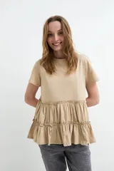 Remera de algodón color beige, con cuello redondo, mangas cortas y diseño peplum con volados fruncidos en la parte inferior.