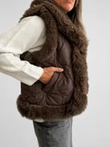 Chaleco acolchado color marrón con diseño matelassé y amplias solapas de piel sintética en tono chocolate. Presenta un corte recto y sin mangas, ideal para superposiciones.