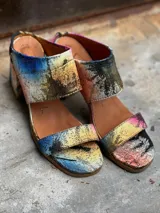 Sandalias de tacón alto con diseño de dos tiras anchas, confeccionadas en tela con estampado abstracto en tonos dorados y negros. Presentan un tacón cuadrado forrado en el mismo tejido.
