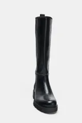Bota de caña alta estilo plano, confeccionada en material sintético negro con acabado liso. Presenta detalle de pespuntes verticales en el cuerpo, punta redonda, suela track dentada y tirador trasero para facilitar el calce.