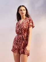 Mono corto negro con estampado en tonos rosados y rojos, cuello camisero, manga corta y lazo ajustable en la cintura.