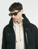 Campera puffer de corte largo, color verde militar, con capucha fija, cierre frontal y puños elásticos internos.