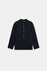 Chaqueta de punto color negro con cuello redondo, manga larga y cierre frontal con botones dorados. Presenta un corte entallado con bajo en evasé.