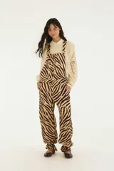 Jardinero largo confeccionado en denim con estampado animal print de cebra en tonos beige y marrón. Presenta tiradores regulables, cierre frontal con botones, bolsillos laterales y piernas amplias con ajuste en los tobillos.