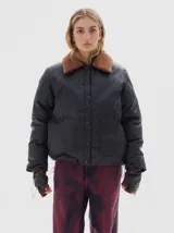 Campera negra acolchada, con cuello de piel sintética marrón, cierre de botones a presión y bolsillos frontales. Incluye mitones a juego con detalles bordados.