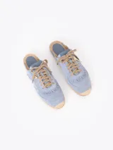 Slide estilo alpargata confeccionado en cuero descarne color celeste, con cordones beige, detalles de flecos y dijes colgantes, sobre una base de yute trenzado.