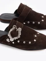Slide de cuero descarne color marrón, con diseño de punta cerrada, detalle de tachas metálicas y hebilla decorativa en el empeine.