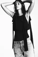 Body negro de cuello barco y tirantes con aplicación de lazos a tono. Cierre en bajo con botones a presión y en espalda con cremallera.