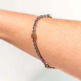 Pulsera plateada de acero quirúrgico con eslabones trenzados y detalles dorados.