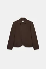 Blazer de corte estructurado en color marrón chocolate, con cuello solapa, hombros marcados y cierre frontal cruzado con botón oculto. Presenta un bolsillo superior tipo ojal y un diseño de bajo redondeado.