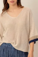 Sweater de punto beige, con escote en V holgado, mangas tres cuartos y detalles de ribetes en tono marrón y azul marino en los puños.