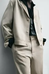 Sobrecamisa de hombre color beige claro, con cuello de solapas de pico, manga larga y cierre frontal de botonadura. Presenta bolsillos de vivo en la cadera.