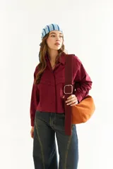 Camisa de corte boxy y calce holgado, color bordó, con cuello clásico, cierre frontal de botones y detalle de tablas con recortes diagonales en el pecho.