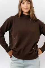 Sweater de tejido de punto color marrón, con cuello alto, corte relajado y terminaciones en rib en puños y cintura. Presenta una hilera de botones metálicos decorativos en uno de los laterales.