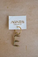 Aro individual dorado con dije colgante en forma de letra "G" con textura irregular.