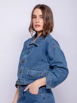 Campera corta de jean color blanco, con cuello camisero, botones metálicos plateados en el frente y puños, y bolsillos delanteros con solapa.