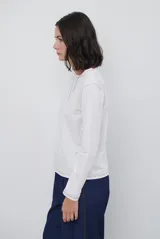 Remera de manga larga color marrón, con costuras a la vista en color blanco que resaltan los cortes de la prenda. Presenta un pequeño bordado blanco en la parte inferior y un corte recto.