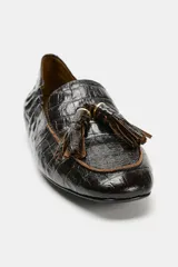 Mocasín de mujer en cuero con textura de piel de cocodrilo, color negro. Presenta detalle de borlas en el empeine, ribetes en contraste y punta redonda.