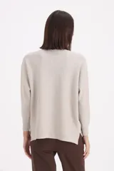 Sweater de tejido de punto color beige, con cuello redondo y detalle de botones negros decorativos en el frente. Presenta mangas largas con puños acanalados y un corte recto.