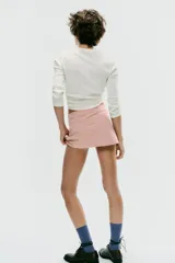 Falda mini de tiro bajo color rosado con estampado de rayas verticales. Presenta dos bolsillos de parche en el frente con detalles de cordones cruzados ajustables y cierre lateral con cremallera oculta.