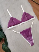 Conjunto de lencería compuesto por un bralette triangular y una tanga, confeccionados en encaje color fucsia con terminaciones y breteles en color crema. El bralette presenta un diseño sin aros con bordes festoneados, mientras que la tanga cuenta con tiras laterales regulables.