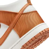 Championes Nike Dunk High de caña alta, con diseño bicolor en blanco y naranja. Presentan una estructura robusta con paneles de tela y cuero sintético, el icónico logo Swoosh en los laterales y suela de goma con tracción.