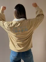 Buzo tipo chomba de corte oversize con diseño a rayas horizontales celestes y blancas. Presenta cuello camisero blanco y un bordado en la espalda con la inscripción República Oriental del Uruguay.