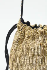 Cartera tipo saco de tamaño pequeño, confeccionada con tejido brillante en color dorado. Presenta cierre mediante cordones ajustables con borlas negras en los extremos y una correa larga de hombro con detalles decorativos y borlas adicionales.