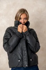 Campera puffer de acabado satinado en color beige, con cuello alto, cierre frontal y bolsillos laterales. Presenta un diseño moderno y sofisticado.