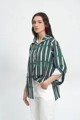 Camisa de corte holgado confeccionada en crepé fino, con estampado geométrico de rayas verticales en tonos verde, blanco y negro. Presenta cuello camisero de tamaño ligeramente ampliado, cierre frontal con botones y mangas largas con puños anchos.