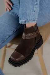 Bota corta de cuero gamuzado color marrón chocolate, con punta cuadrada y suela track. Presenta una correa con hebilla desmontable y cierre lateral con cremallera.