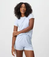 Blusa de pijama de mujer color celeste, confeccionada en tejido peach touch de poliéster con elastano, con estampado de moños sutiles. Presenta cuello redondo, mangas cortas con detalles de encaje blanco y un pequeño moño decorativo en el escote.