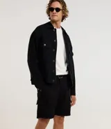 Bermuda cargo negra confeccionada en sarga de algodón, con cintura tradicional, cierre de cremallera y botón, y bolsillos laterales útiles.