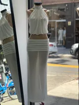 Conjunto de dos piezas color blanco compuesto por un top halter con frunces y una falda larga de tiro bajo con cintura fruncida.