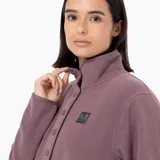 Buzo polar de microfleece color rosa viejo, con cuello alto, cierre frontal parcial con botones a presión y bolsillo frontal tipo canguro. Presenta detalles en nylon en la tapeta y los bolsillos, y puños con sujeción elástica.
