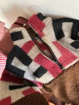 Buzo de diseño único confeccionado con una combinación de corderito marrón y paneles de tejido vintage con estampado geométrico en tonos gris, negro y bordó. Presenta cuello alto con cierre frontal y mangas largas.