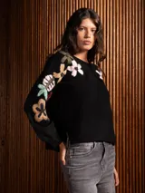 Buzo de cuello redondo en color gris, con mangas largas y diseño holgado. Presenta un bordado floral multicolor con detalles de cuentas en la parte frontal y en las mangas.