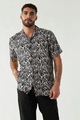Camisa de manga corta con cuello cubano, confeccionada en viscosa con estampado de hojas en tonos azules. Presenta cierre frontal abotonado y corte slim.