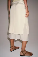 Falda midi de tiro medio, color beige, con detalle de combinación de tejidos a contraste y volante plisado semitransparente en el bajo. Cuenta con cierre lateral de cremallera oculta.