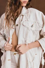 Campera oversize de jean color crudo, con cuello clásico, cierre frontal de botones metálicos, bolsillos con solapa y detalles de roturas con terminaciones deshilachadas.